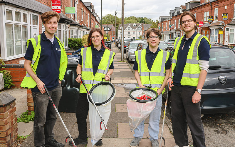a photo of 4 community ambassadors standing in the street smiling to the camera holding litter pickers and waste bags