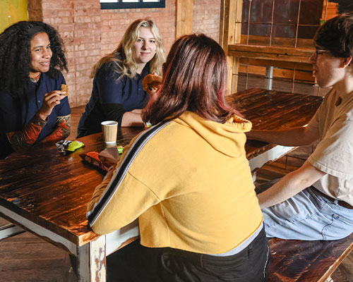 a photo of 2 community ambassadors sat at a table talking to 2 students