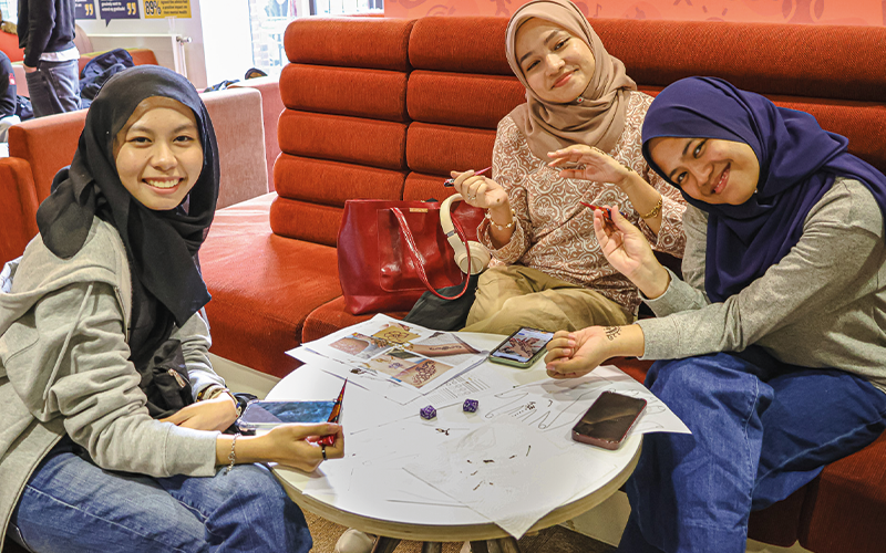 a photo of students sat at a table doing crafts smiling at the camera 