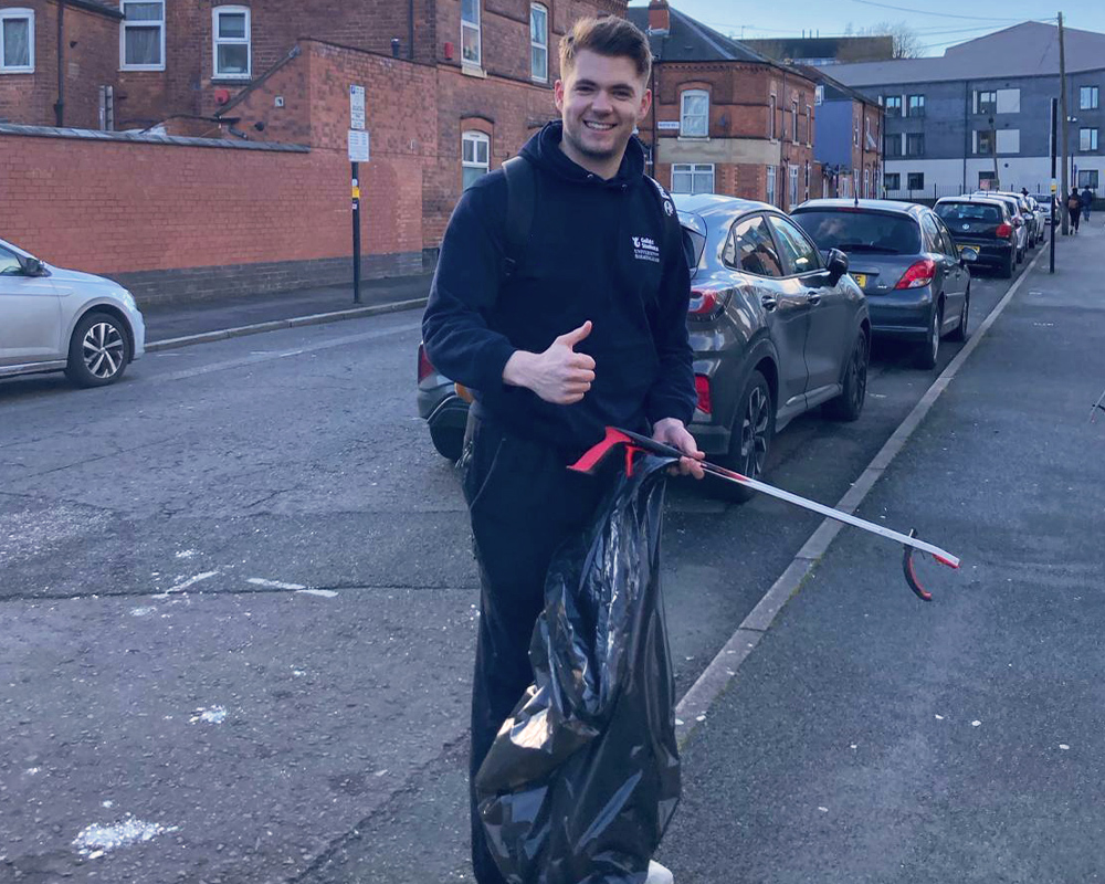 a student holding a bin bag whilst picking up rubbish in the street
