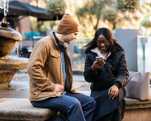 2 students sat at mermaid fountain with one on their phone